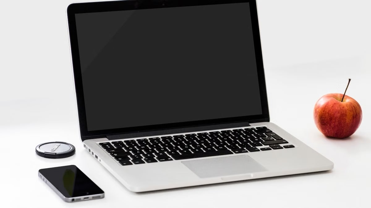 A minimalist workspace featuring a laptop, smartphone, and an apple on a clean white desk.